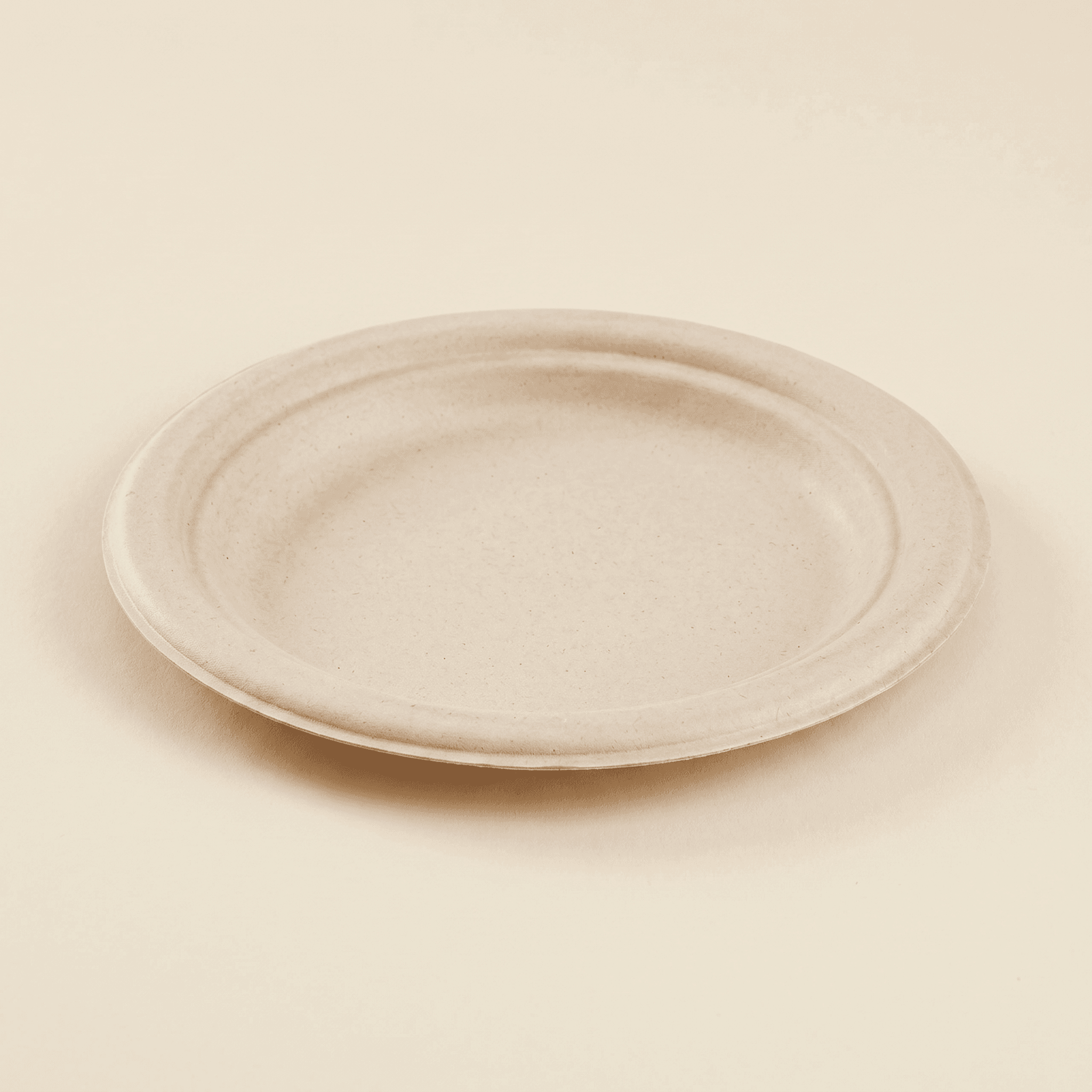 7-inch round bagasse plate at a three-quarter angle on a cream studio background, showing the wide flat rim with its raised concentric rim ring and the shallow molded sugarcane fiber well