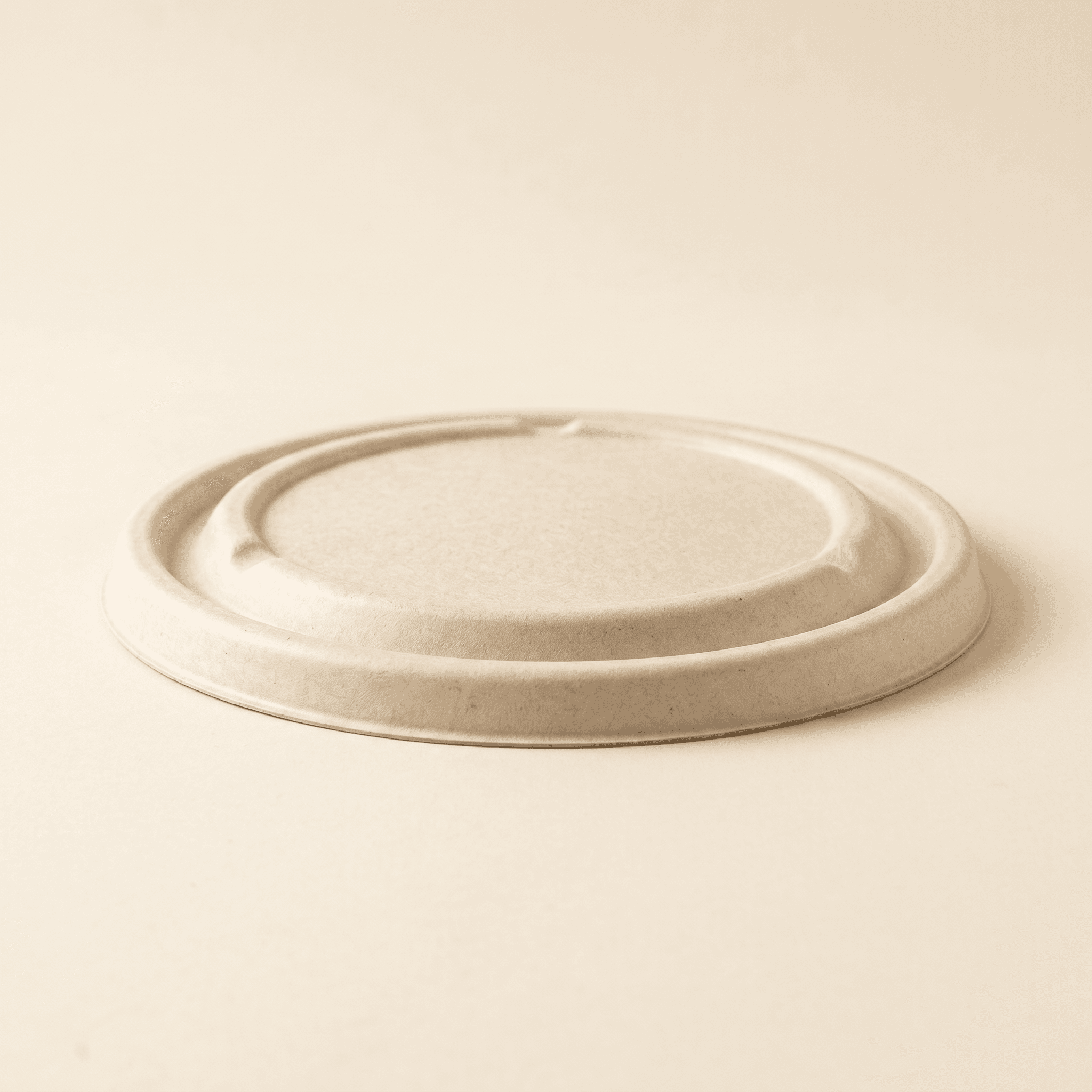 Side profile of the bagasse fiber lid on a cream studio surface, showing its low dome and the rounded rolled snap-over rim