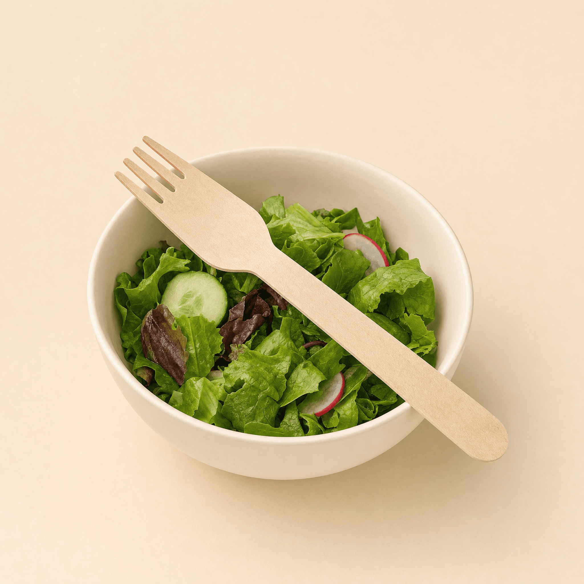 Birch fork resting across a plain cream bowl of fresh green salad on a cream background